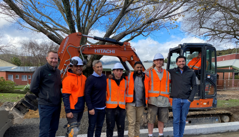 Seven people standing in front of a digger