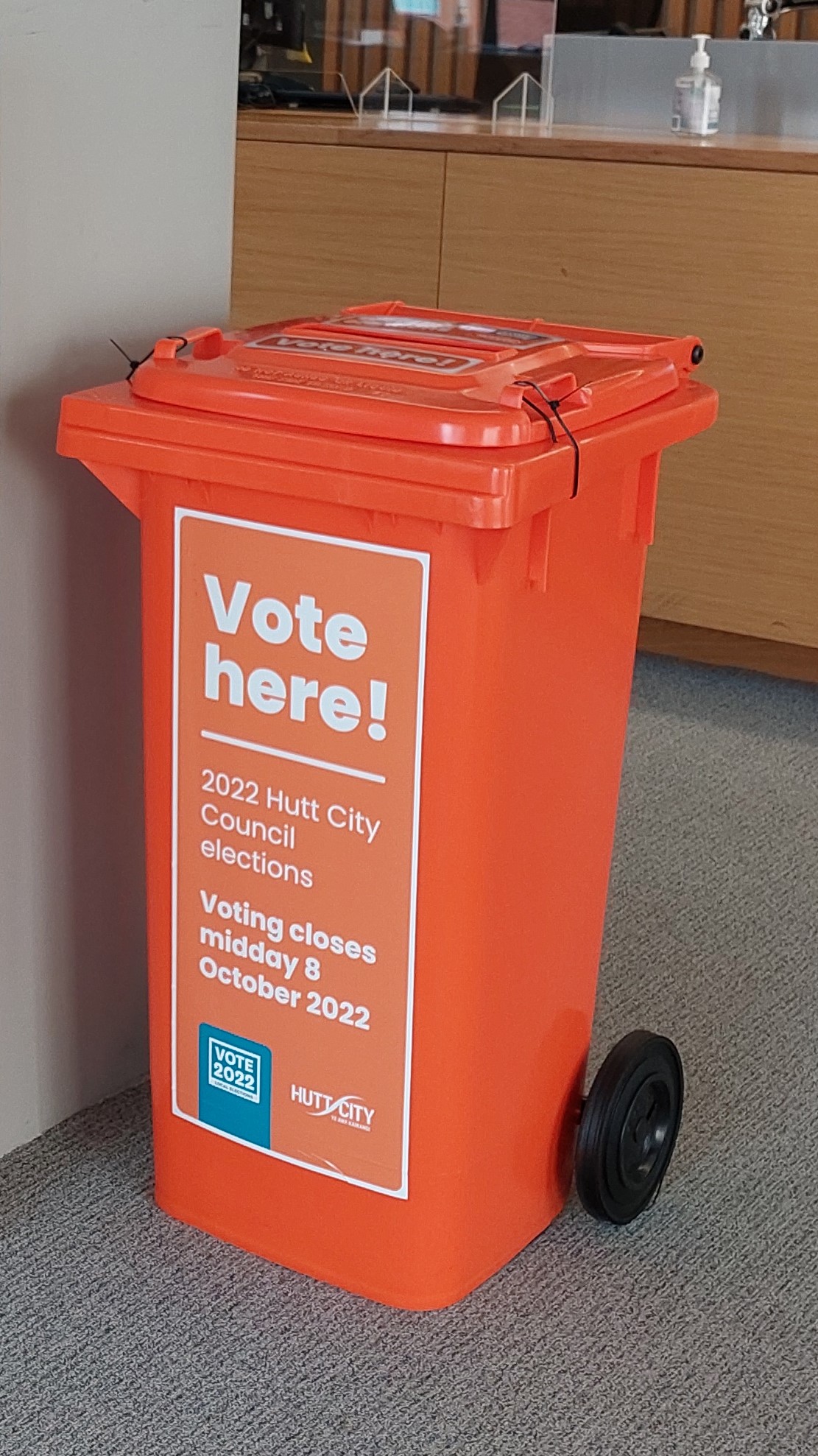 An orange wheelie bin with Vote here! on the side and a ballot hole in the top.