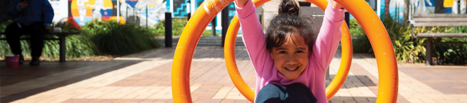 child smiling and playing on circular metal bike parks banner image